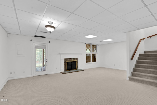 unfurnished living room featuring carpet floors, visible vents, stairway, a brick fireplace, and a drop ceiling