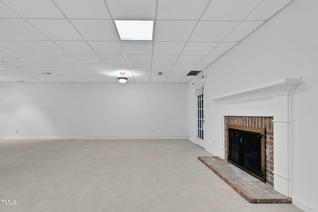 unfurnished living room featuring a brick fireplace, carpet flooring, a drop ceiling, and baseboards