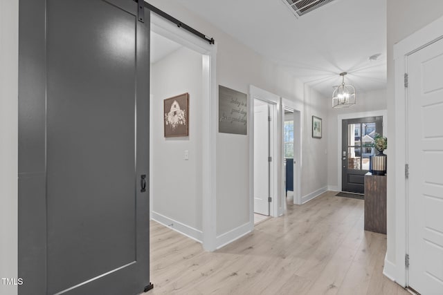 hallway with light wood-type flooring, visible vents, baseboards, and a barn door