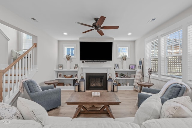 living area featuring light wood finished floors, recessed lighting, visible vents, a glass covered fireplace, and stairs