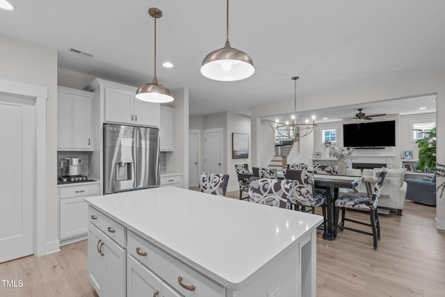 kitchen featuring stainless steel fridge, a kitchen island, decorative light fixtures, light countertops, and white cabinetry