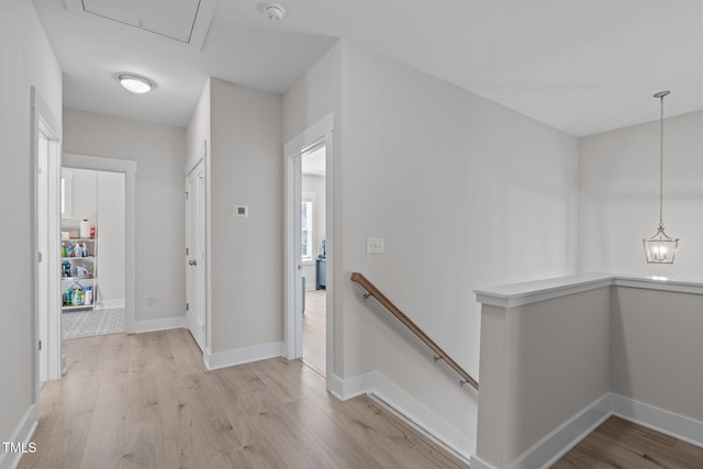 hall featuring baseboards, light wood-style flooring, and an upstairs landing