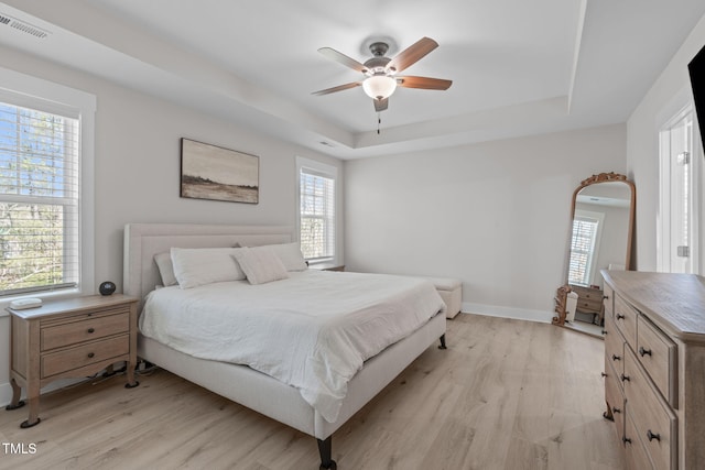 bedroom with light wood-type flooring, a raised ceiling, and visible vents