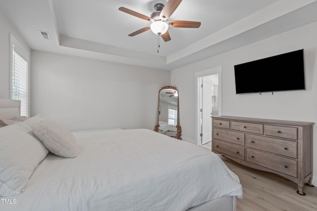 bedroom featuring ceiling fan, a tray ceiling, light wood-type flooring, and visible vents