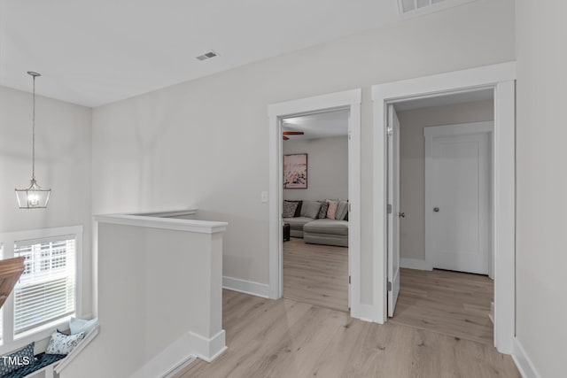 hall with a chandelier, visible vents, baseboards, an upstairs landing, and light wood-style floors