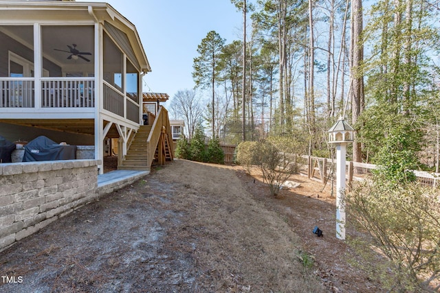 view of yard featuring ceiling fan, stairway, fence, and a sunroom