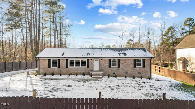 snow covered back of property with crawl space, a fenced backyard, and brick siding