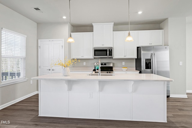 kitchen featuring light countertops, appliances with stainless steel finishes, hanging light fixtures, and a center island with sink