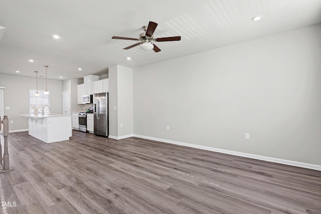 unfurnished living room with baseboards, ceiling fan, wood finished floors, a sink, and recessed lighting