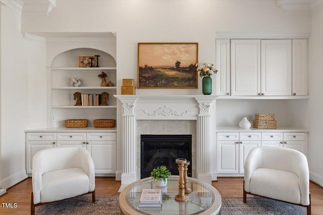 living area with built in features, crown molding, a fireplace, wood finished floors, and baseboards