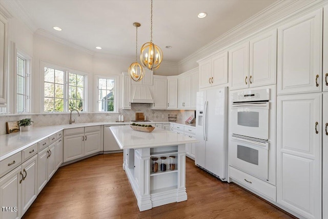 kitchen with light countertops, custom range hood, a kitchen island, wood finished floors, and white appliances