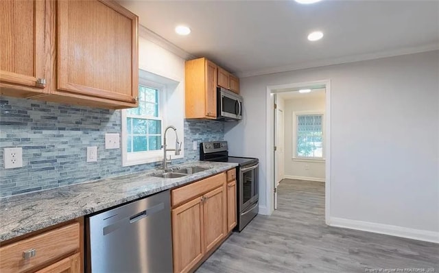 kitchen featuring baseboards, light stone counters, ornamental molding, stainless steel appliances, and a sink