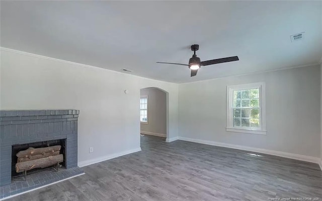 unfurnished living room with arched walkways, a brick fireplace, baseboards, and wood finished floors