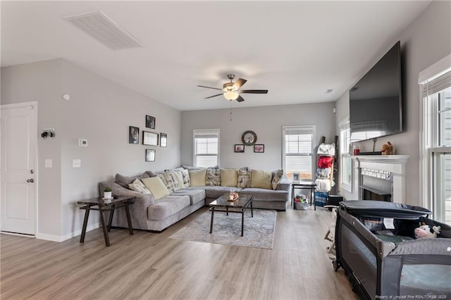 living area with light wood-type flooring, visible vents, a fireplace, and ceiling fan