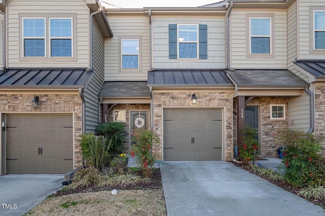 view of property with a standing seam roof, concrete driveway, a garage, and stone siding