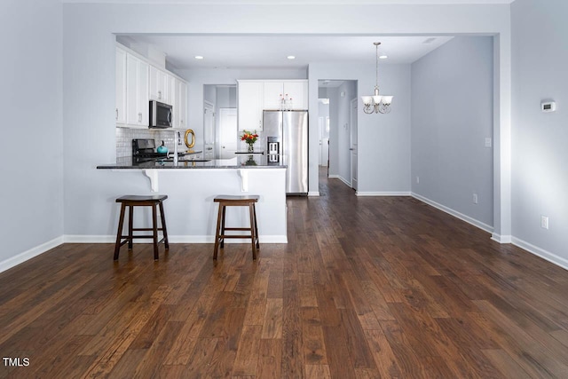 kitchen featuring a breakfast bar, an inviting chandelier, a peninsula, stainless steel appliances, and dark wood-type flooring