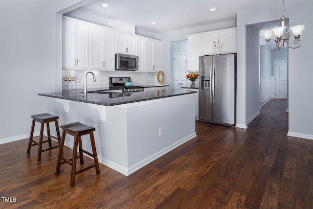 kitchen with a sink, dark stone countertops, appliances with stainless steel finishes, a peninsula, and dark wood-style flooring