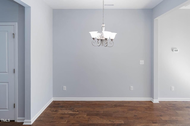 empty room with visible vents, a notable chandelier, wood finished floors, and baseboards