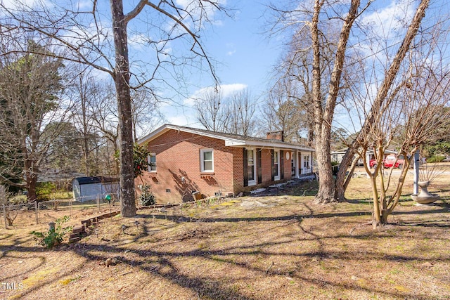 exterior space with an outbuilding, a storage shed, brick siding, crawl space, and a chimney