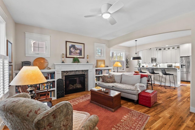 living room with a fireplace, light wood-type flooring, and ceiling fan