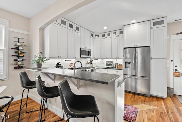 kitchen with stainless steel appliances, light wood-style floors, a peninsula, and decorative backsplash