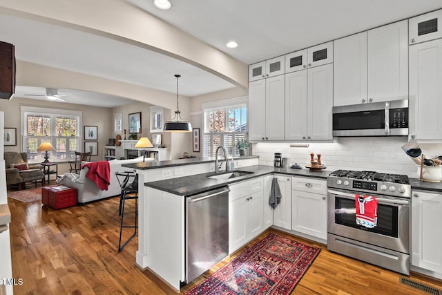 kitchen with open floor plan, a kitchen bar, appliances with stainless steel finishes, a peninsula, and a sink