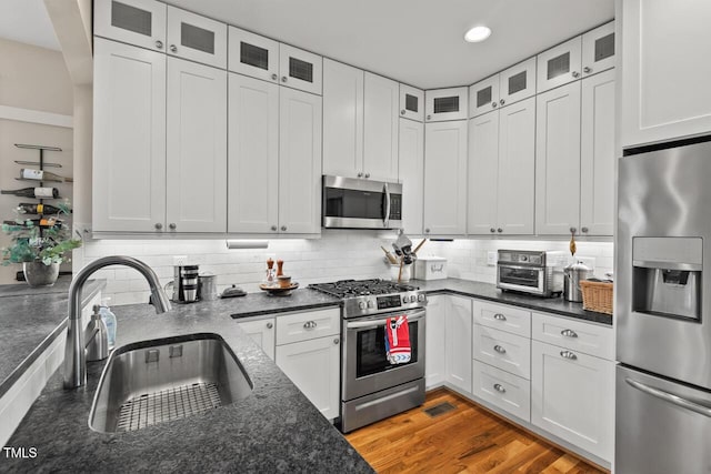 kitchen featuring light wood finished floors, backsplash, appliances with stainless steel finishes, white cabinetry, and a sink