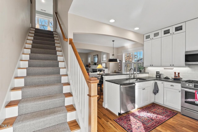 kitchen featuring dark countertops, light wood-type flooring, appliances with stainless steel finishes, a peninsula, and a sink