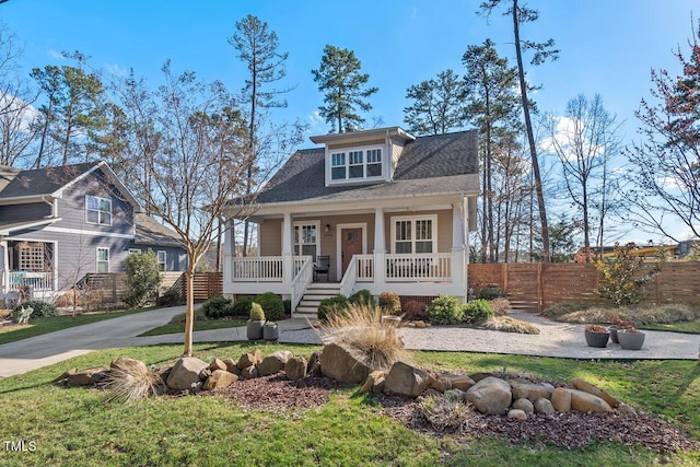 view of front of home with covered porch, a shingled roof, and fence