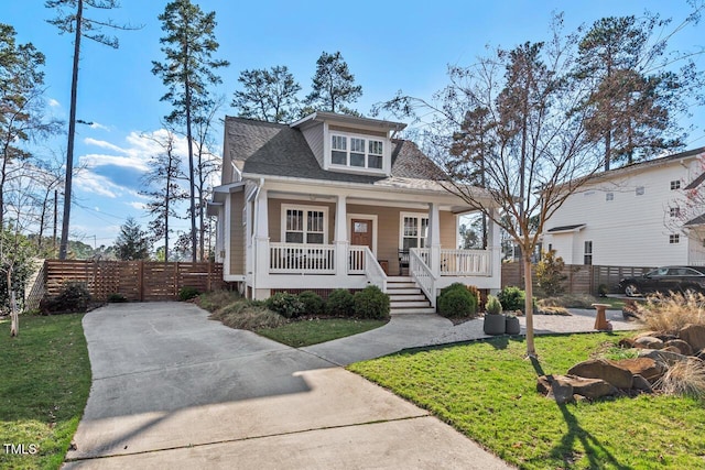 bungalow with roof with shingles, covered porch, a front lawn, and fence