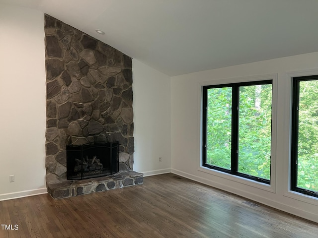 unfurnished living room with a stone fireplace, visible vents, baseboards, vaulted ceiling, and dark wood finished floors