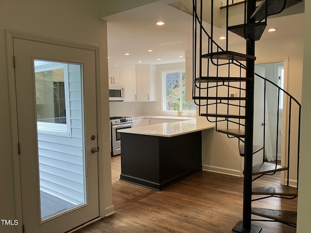 kitchen with white microwave, wood finished floors, light countertops, white cabinetry, and stainless steel range with gas stovetop