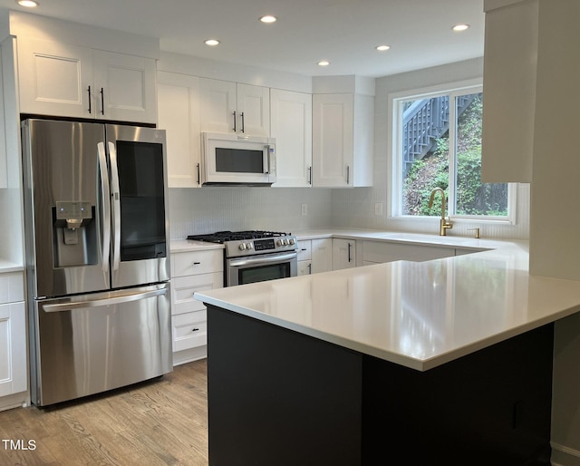 kitchen with appliances with stainless steel finishes, light countertops, light wood-type flooring, white cabinetry, and backsplash