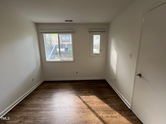 spare room featuring dark wood-type flooring, visible vents, and baseboards