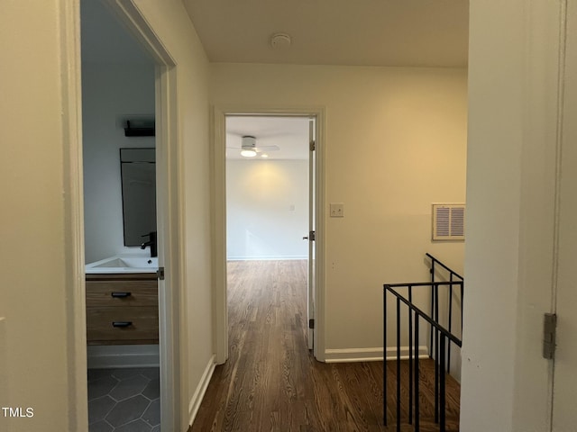 hall featuring a sink, an upstairs landing, visible vents, baseboards, and dark wood-style floors