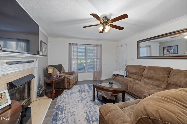 living room featuring crown molding, light wood finished floors, a textured ceiling, a tile fireplace, and baseboards