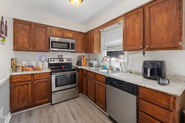 kitchen featuring light stone counters, light wood-style flooring, appliances with stainless steel finishes, brown cabinetry, and a sink