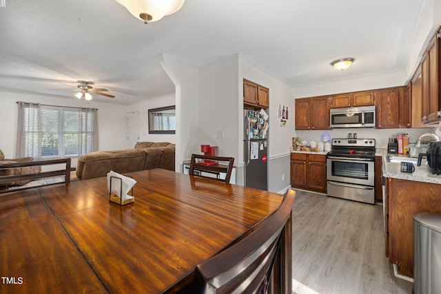 kitchen featuring brown cabinetry, open floor plan, stainless steel appliances, crown molding, and light wood-type flooring