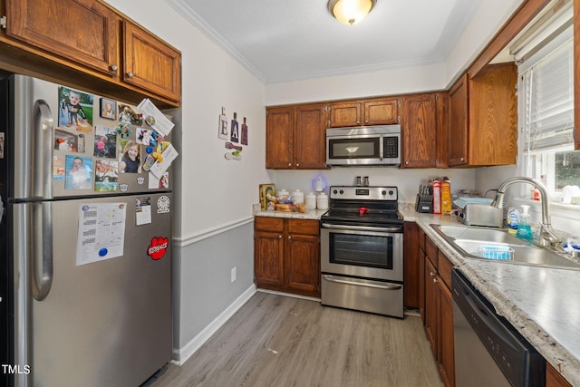 kitchen with a sink, light countertops, appliances with stainless steel finishes, brown cabinets, and light wood finished floors