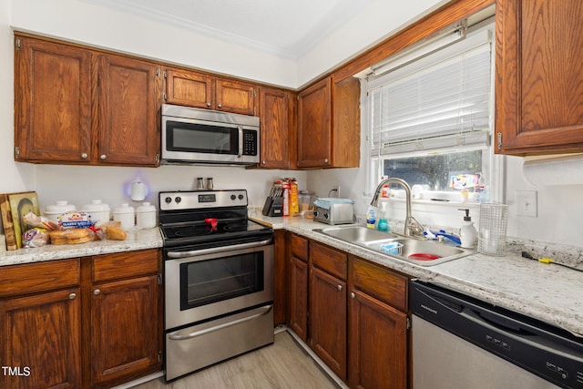 kitchen with stainless steel appliances, light stone counters, brown cabinetry, and a sink