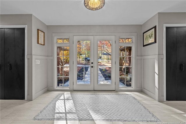 doorway with light tile patterned floors, french doors, wainscoting, and a decorative wall