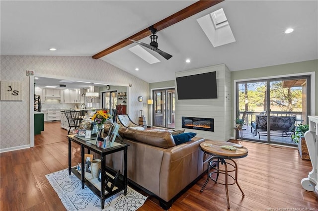 living room featuring lofted ceiling with skylight, a fireplace, wood finished floors, and wallpapered walls