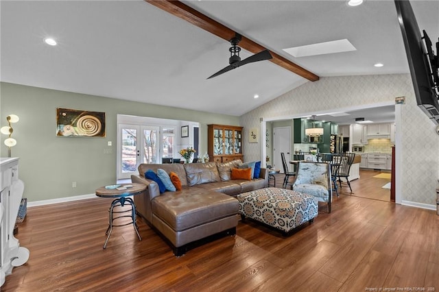 living area featuring wood finished floors, a ceiling fan, baseboards, lofted ceiling with skylight, and wallpapered walls