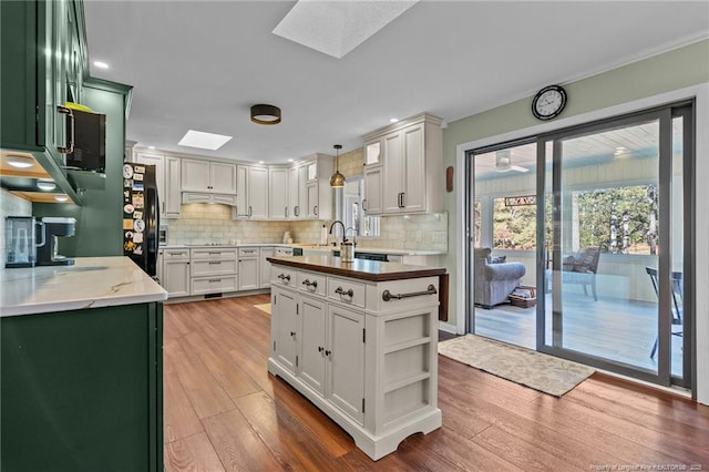 kitchen with a skylight, decorative light fixtures, light wood finished floors, backsplash, and white cabinetry