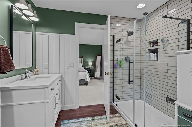 full bathroom featuring ensuite bathroom, wood finished floors, vanity, tiled shower, and wainscoting