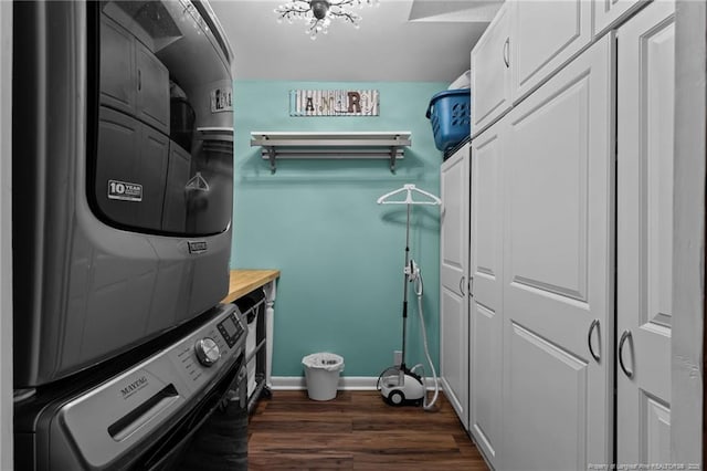 laundry room with dark wood-style flooring, cabinet space, stacked washer and clothes dryer, and baseboards