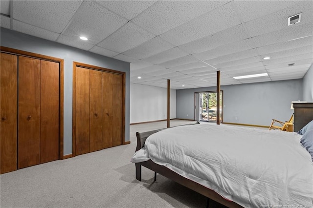 bedroom featuring a drop ceiling, light colored carpet, visible vents, baseboards, and multiple closets