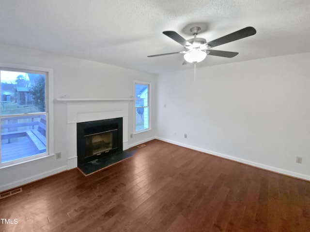 unfurnished living room with visible vents, dark wood finished floors, baseboards, a fireplace with flush hearth, and a textured ceiling