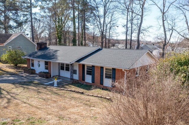 ranch-style home with a shingled roof, a front yard, brick siding, and a chimney