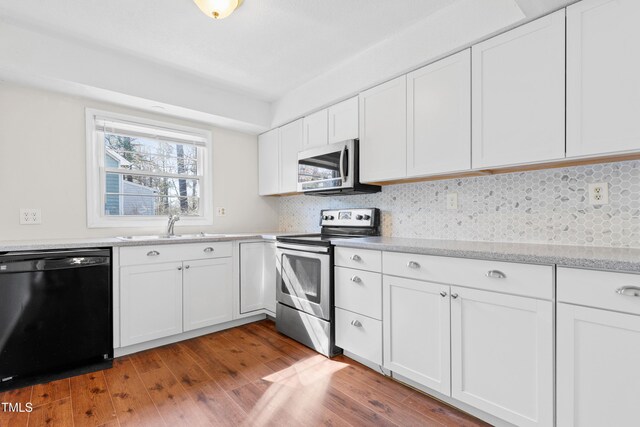 kitchen featuring white cabinets, decorative backsplash, appliances with stainless steel finishes, wood finished floors, and a sink